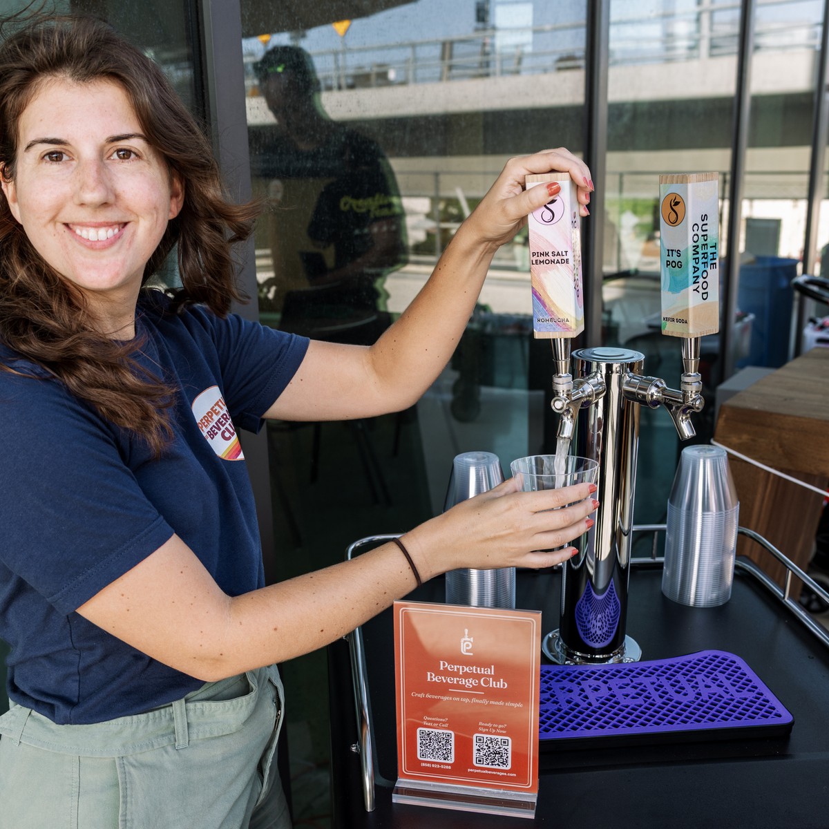 A Perpetual team member pouring The Superfood Company Pink Salt Lemonade kombucha beside It's POG! kefir soda on a two-tap Perpetual kegerator at an event